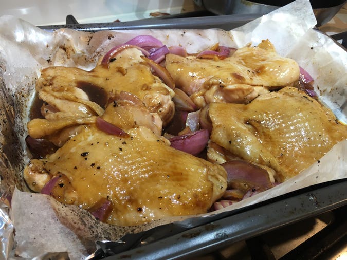 boneless skin-on chicken thighs in tray, baked halfway with the skin down, and now flipped and basted with the glaze