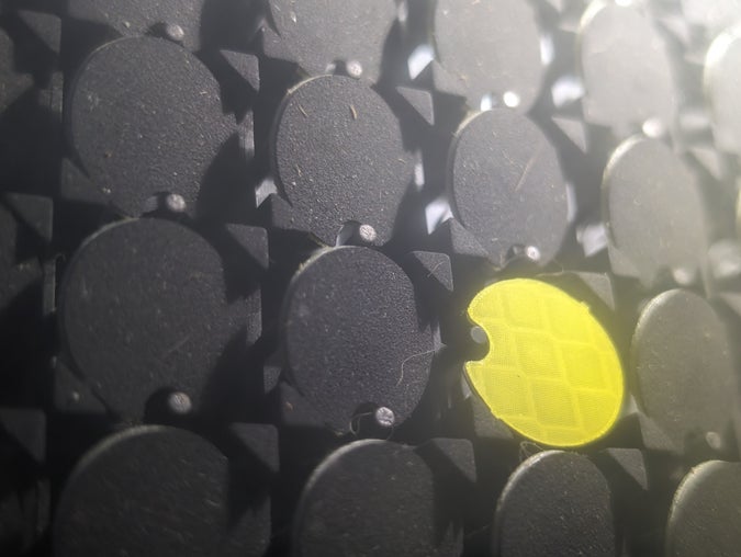 closeup of a grid of flipdots with one turned forwards, revealing its lime-green retroreflective surface