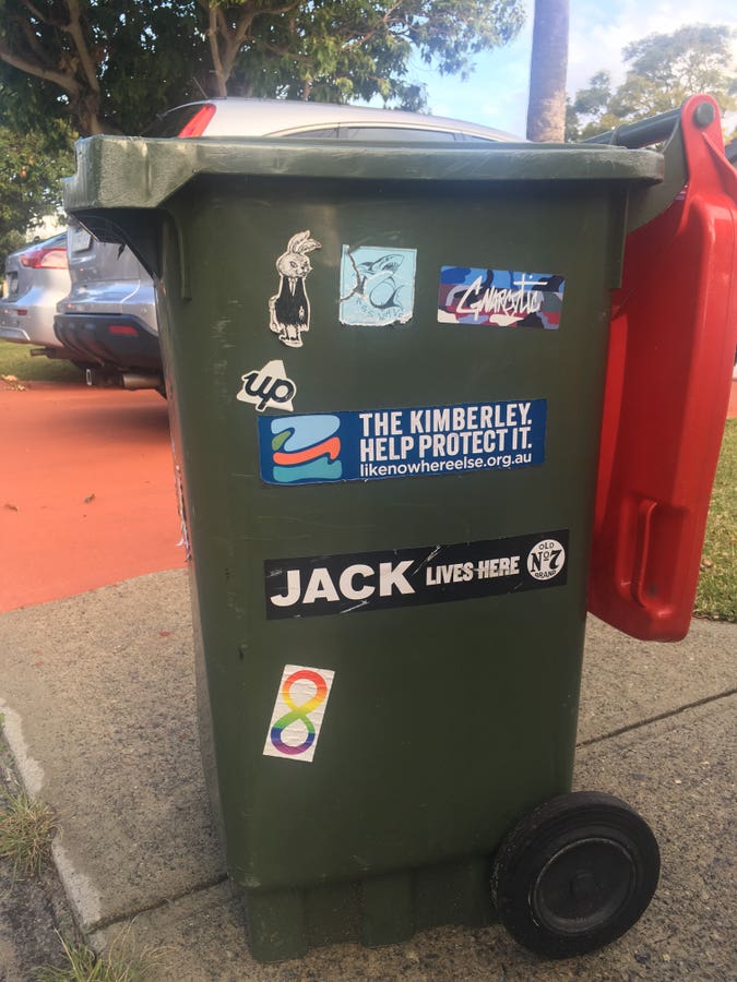 red top wheelie bin, with a “rainbow infinity” autism sticker