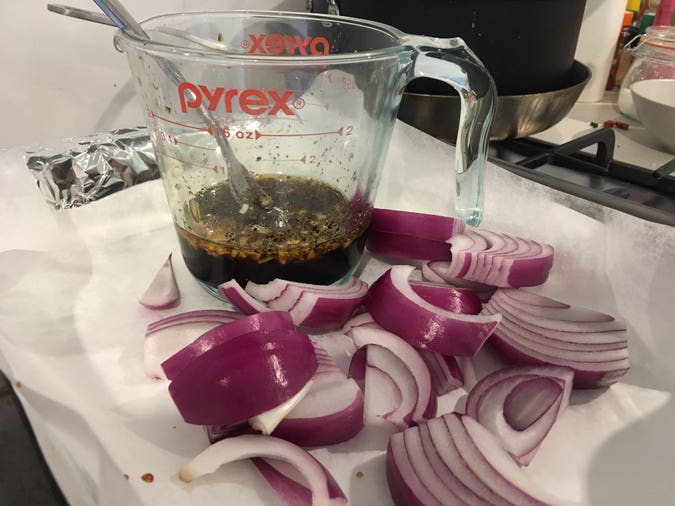 glaze with honey, soy sauce, apple cider vinegar, sesame oil, garlic, and pepper, to be poured into a foil-and-baking-paper-lined tray with cut red onions for a head start before the chicken