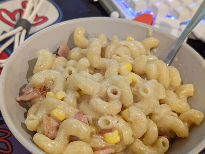 macaroni cheese with corn, onion, and bacon, served in a bowl with a spoon.