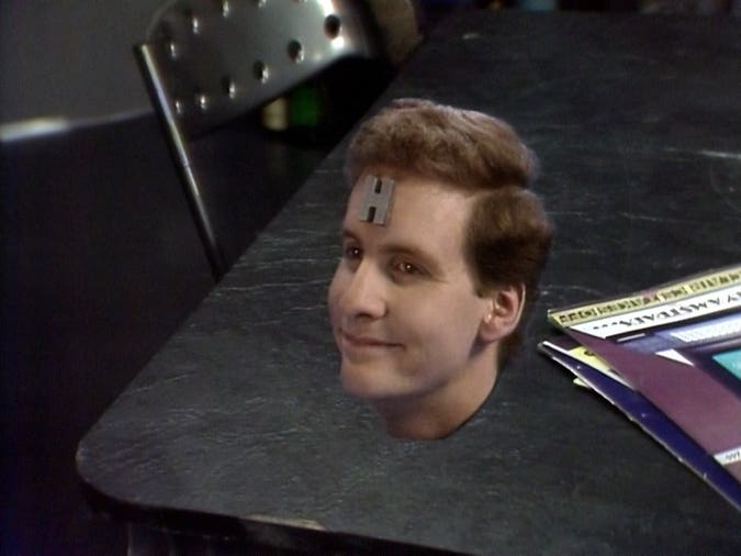 arnold rimmer’s head peeking up through a table